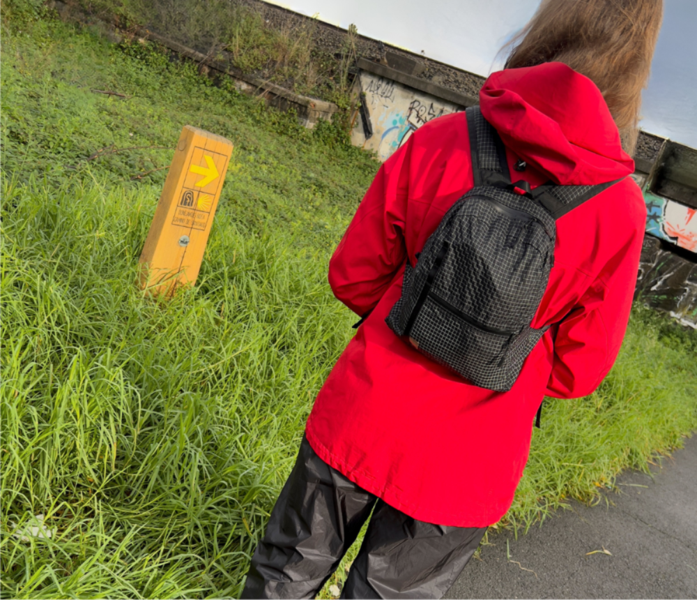 Pilgrim on the Camino de Santiago route looks at mile marker. She is wearing the unisex mini backpack known as The Mighty Mini.