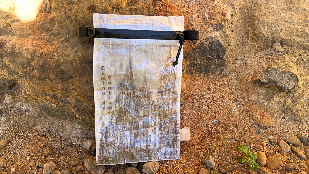 Ultreiatrek Dyneema® Valuable Holder with the Cathedral of Santiago de Compostela on the cover. It is placed on a medieval wall with rocks and stones.